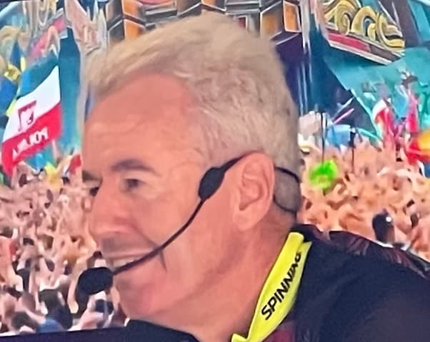 Dave Walls coaching with a headset in front of a lively crowd
